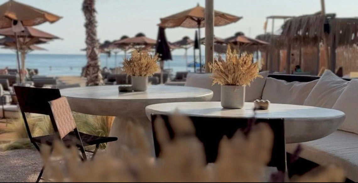 Outdoor dining area with tables, chairs, and decorative elements under a net canopy by the beach.